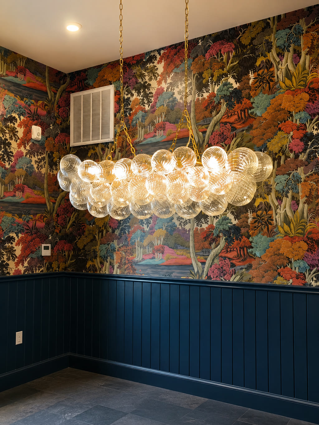 Designer wallcovering installation by RGT Wallpaper — scenic forest mural with bubble-glass chandelier above navy wainscoting
